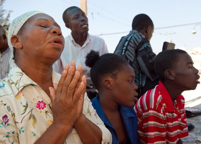Noel Zierne (left) prays during worship outside St. Martin Methodist Church in Port-au-Prince. A UMNS photo by Mike DuBose.