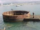 A gun turret rising out of the water from the sunken Arizona Battleship.