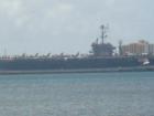 An aircraft carrier makes a stop at Pearl Harbor.  There are many ships and submarines that travel in and out of the harbor daily.