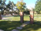 A fairly formal metal and brick fence that surrounds a lovely, traditional red brick home.