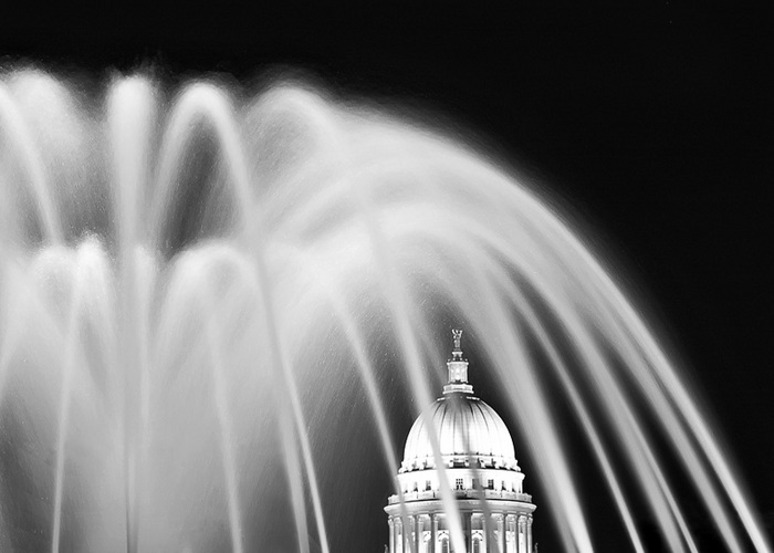 An evening photograph of the Wisconsin State Capitol as it is framed by the fountain on Monona Terrace in Madison, Wisconsin. Large