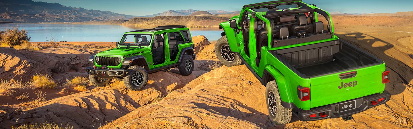 Two green 2026 Jeep Wrangler parked in the desert by a lake