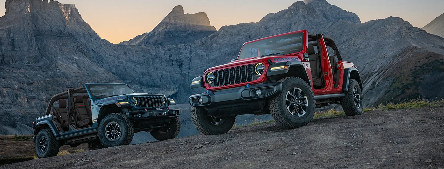 Two 2026 Jeep Wrangler parked on a rocky hill by some mountains