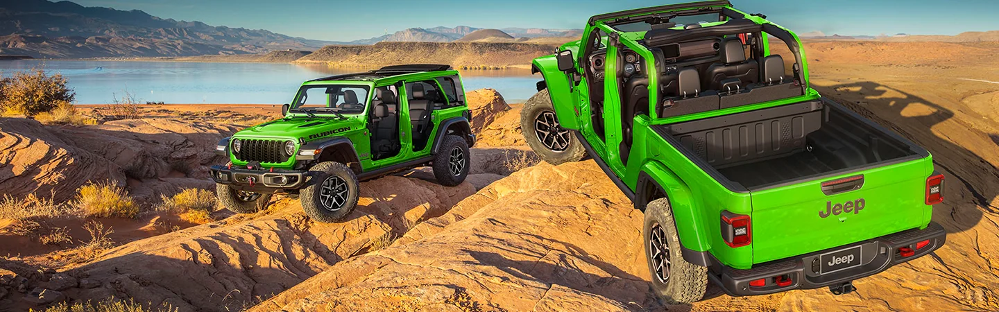 Two parked green 2026 Jeep Wrangler on a rocky hill side by a lake