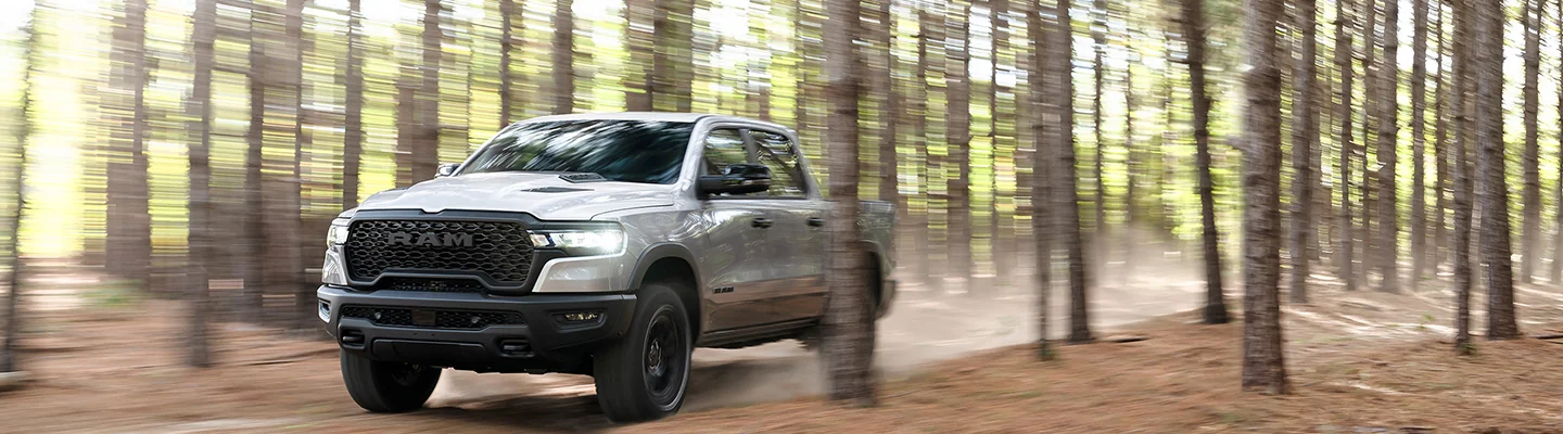 Front view of a gray 2026 RAM 1500 driving though the woods