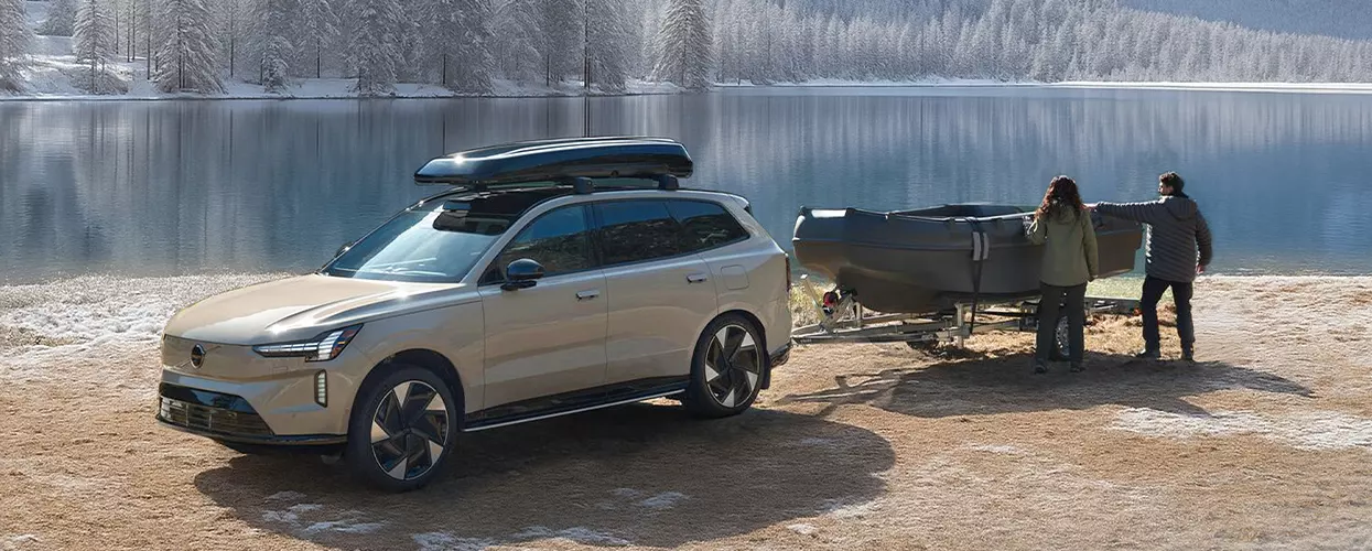A tan 2026 Volvo EX90 parked at a lake with 2 people getting ready to unload there boat