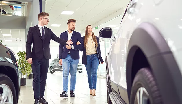 two people discussing cars with a third at a dealership