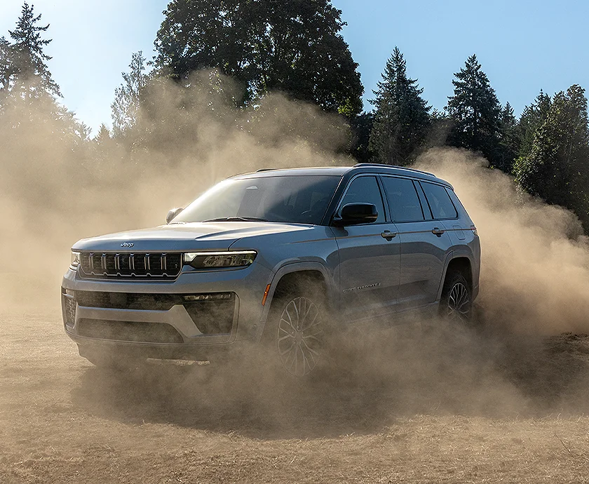 Front side view of a gray 2026 Jeep Grand Cherokee driving though dirt