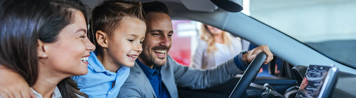 family of three smiling in a car they are shopping at dealership