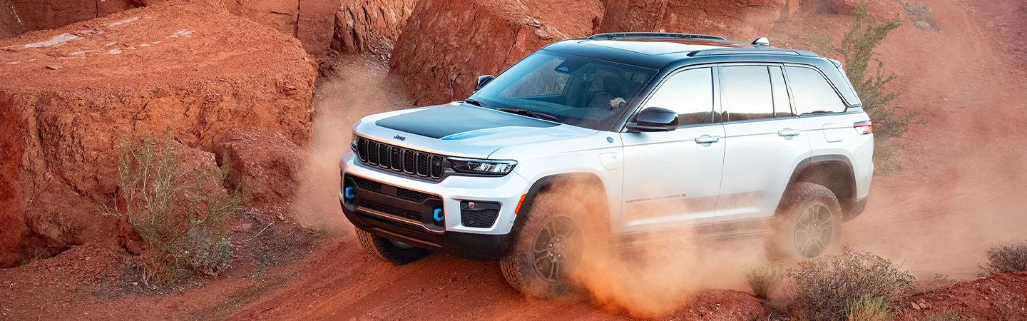 White 2025 Jeep Grand Cherokee driving around kicking up dirt