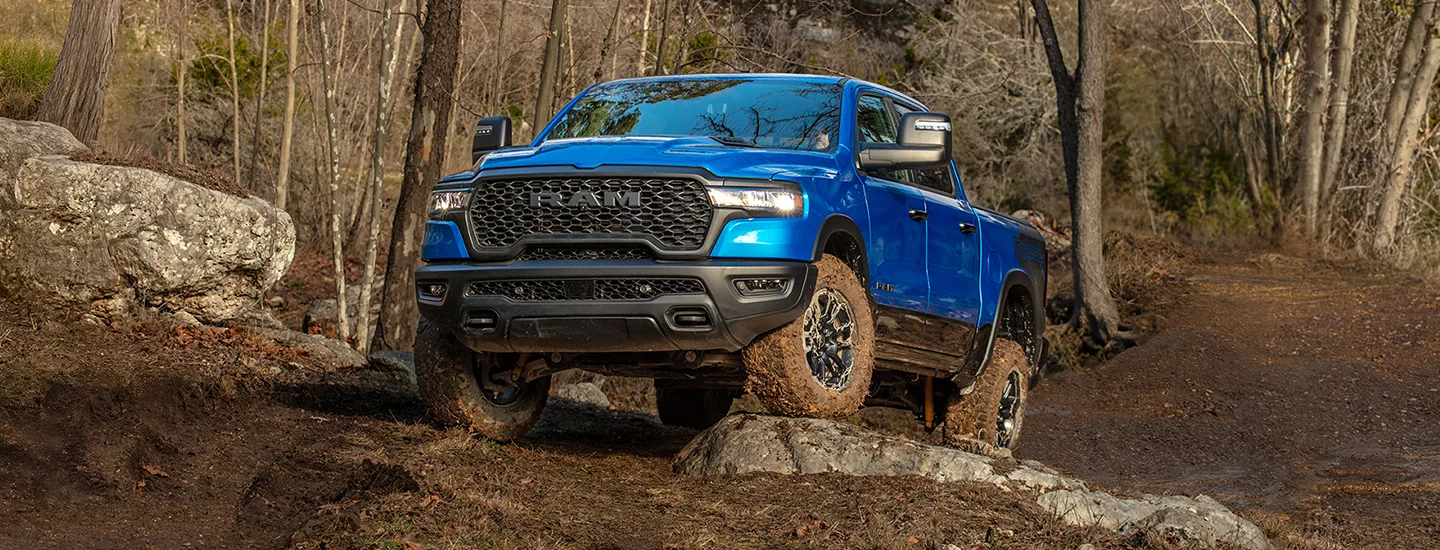 Front view of a blue 2026 RAM 1500 driving off road in the woods