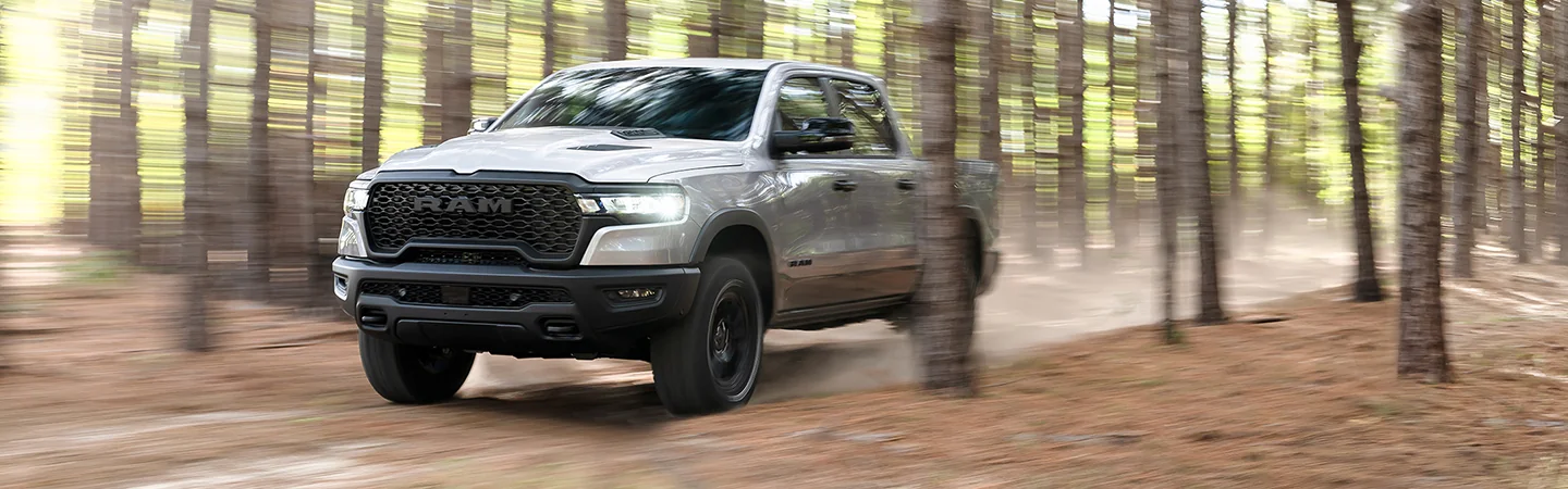 Front view of a gray 2026 RAM 1500 driving fast though the woods