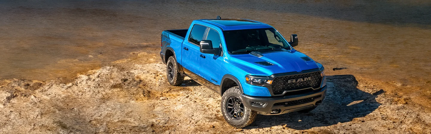 front side view of a blue 2026 RAM 1500 parked on a rocky water front