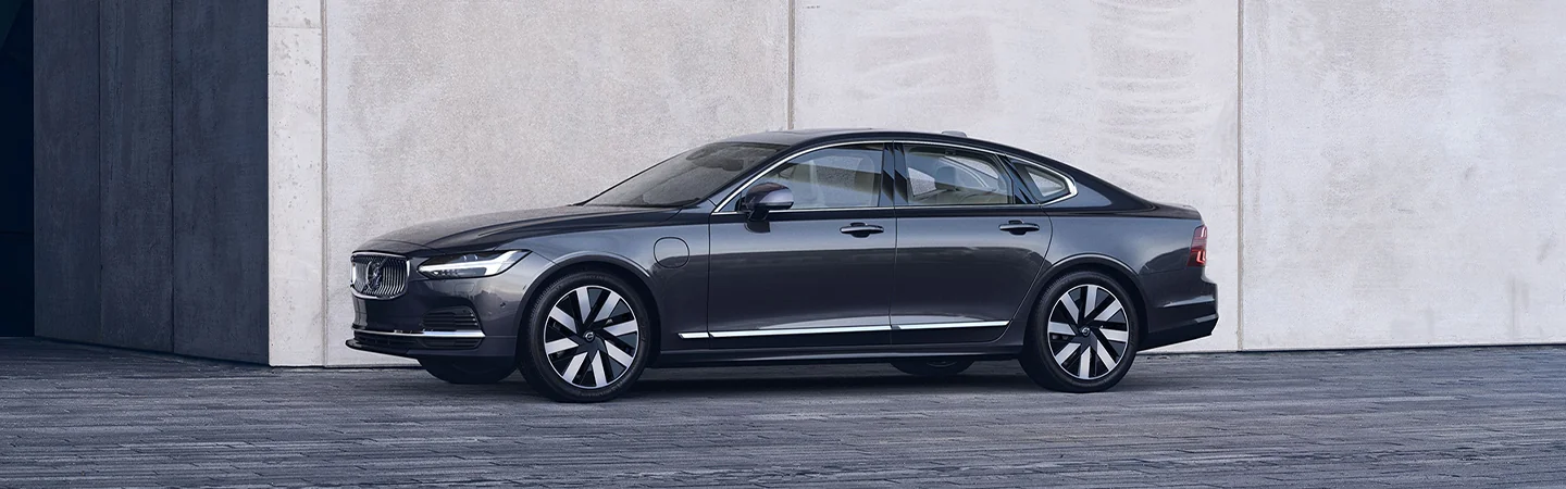 Side view of a parked black 2025 Volvo S90 Hybrid next to a building