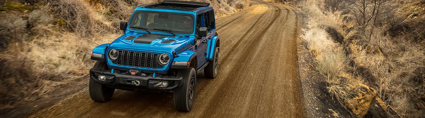 blue Jeep Wrangler driving on a dirt road