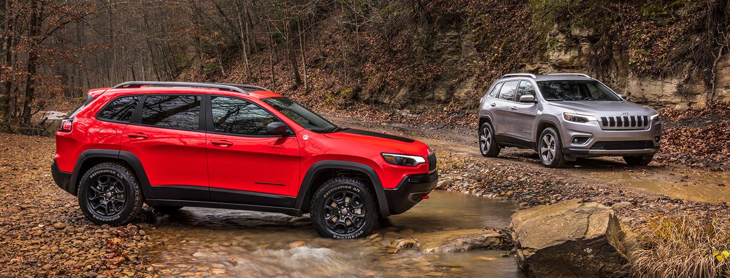 A red and a silver Jeep Cherokee driving over creeks and mud in the woods.