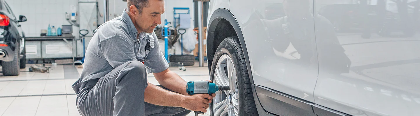 Auto mechanic working on tires with air gun for bolts in hands