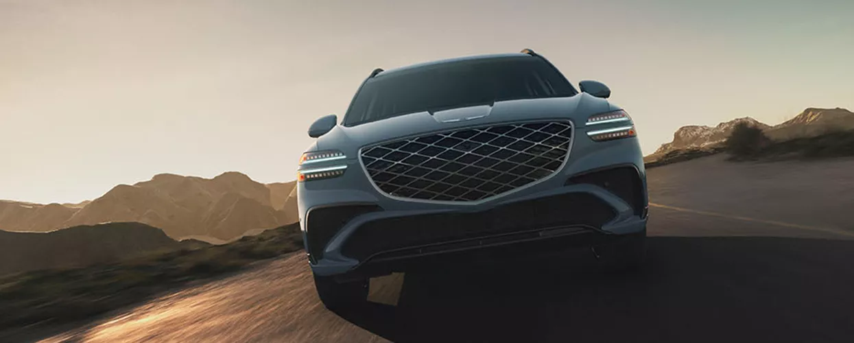 Genesis GV70 driving down a road with mountains in the background