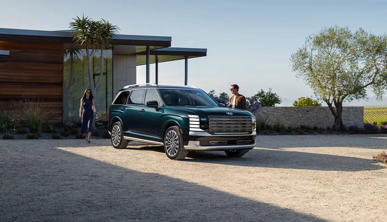 Front view of a parked green Hyundai SUV in a driveway with a couple walking to the car