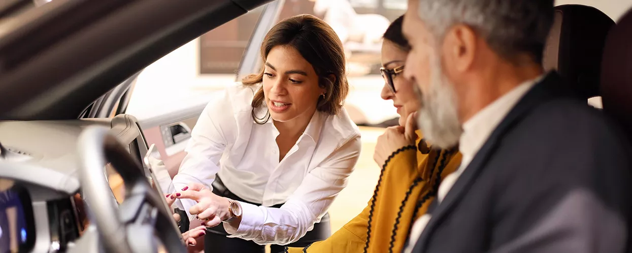 Two people in a car with a car salesman showing them something on a tablet