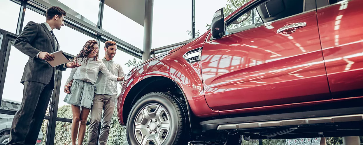 Car salesman showing a couple a new vehicle in a car dealership showroom