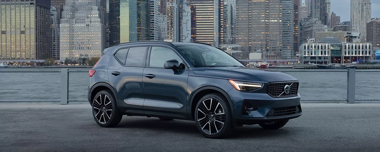 Side view of a parked blue 2026 Volvo XC40 with a city in the background