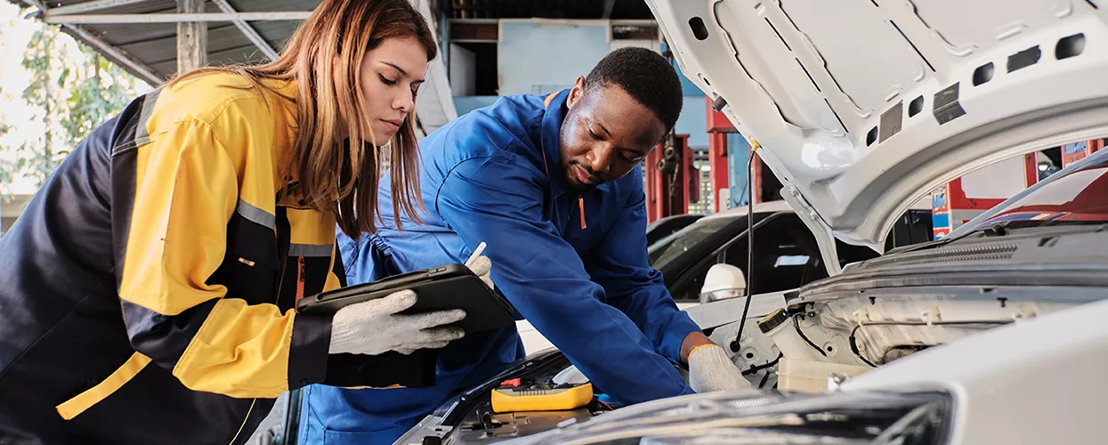 two auto mechanics working on a car while reading text on repair steps