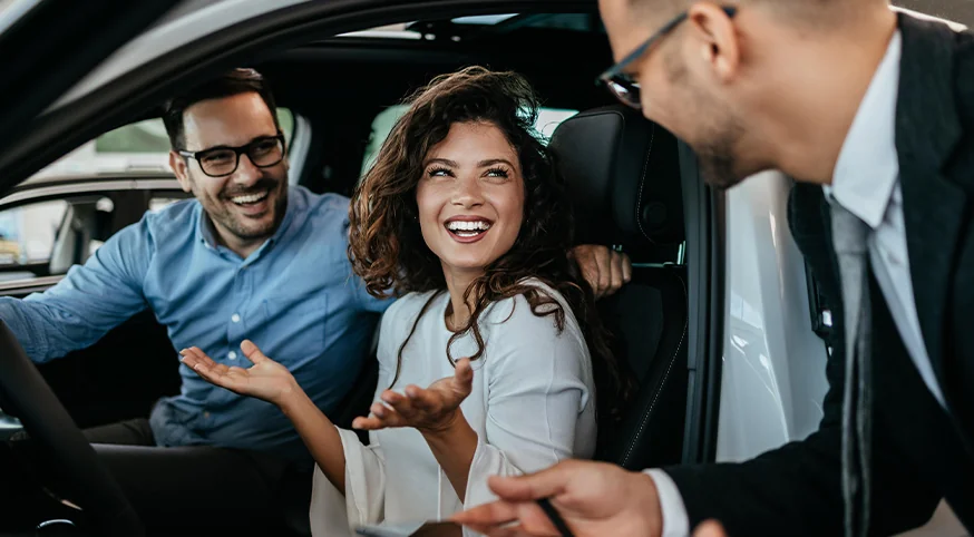 couple in a car speaking with car salesmen standing by door open