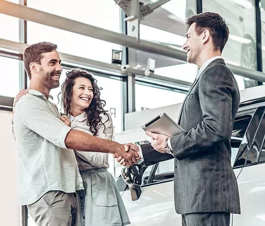 a couple shaking hands wtih salesperson reviewing vehicle financing information