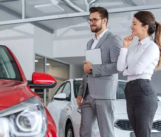 two people looking at Vehicles displayed in a dealership showroom