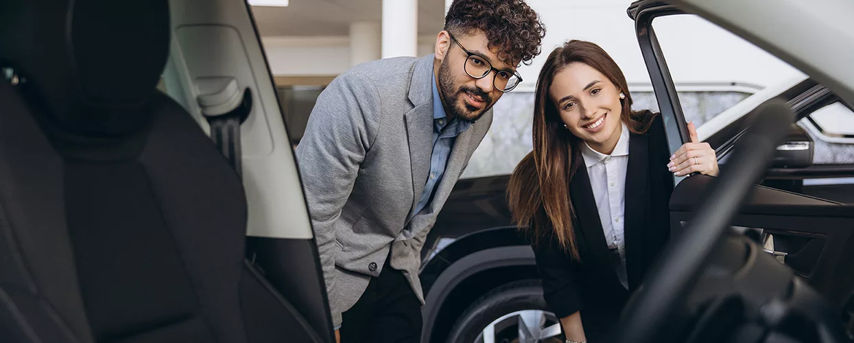 A couple looking inside car and smiling at interior at a dealership