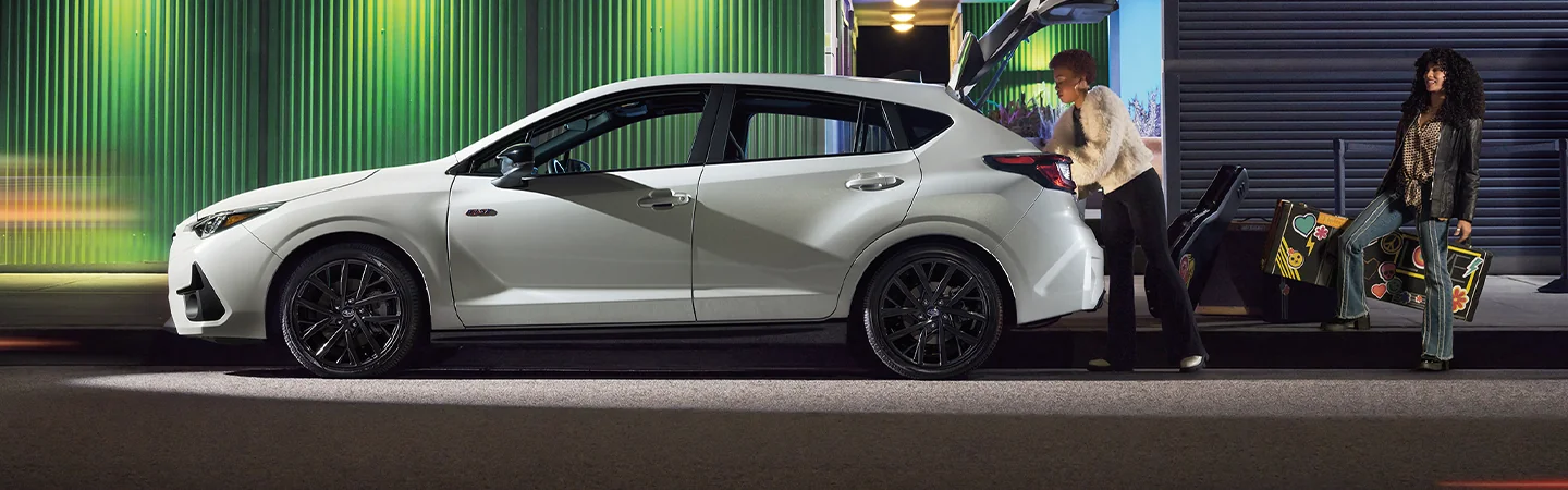 Side view of a parked white 2026 Subaru Impreza with two people loading up band equipment