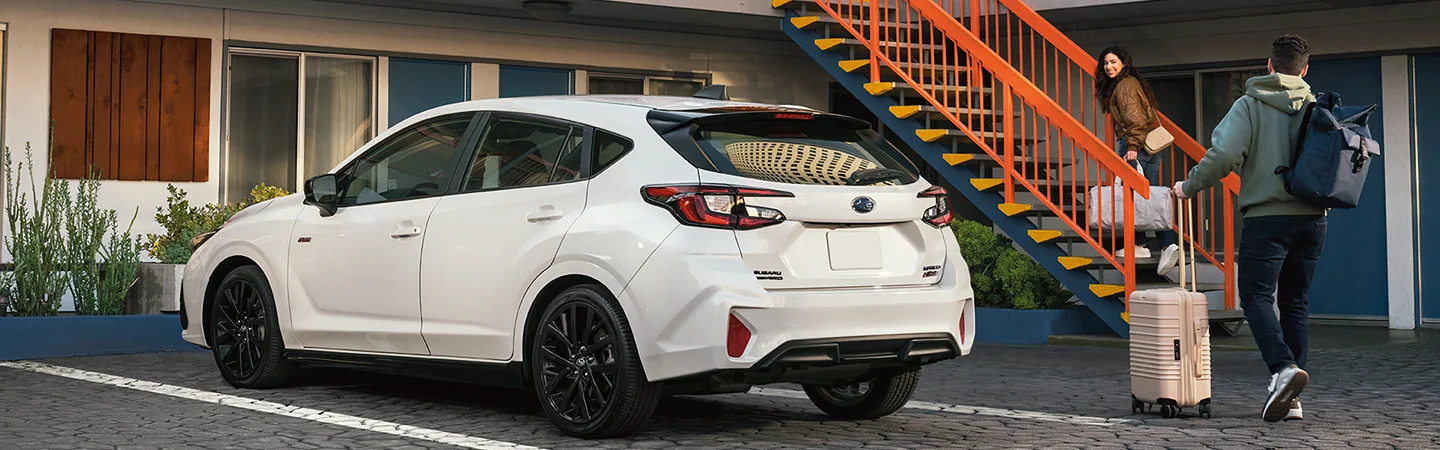Back side view of a parked white 2026 Subaru Impreza with 2 people taking luggage to there hotel room