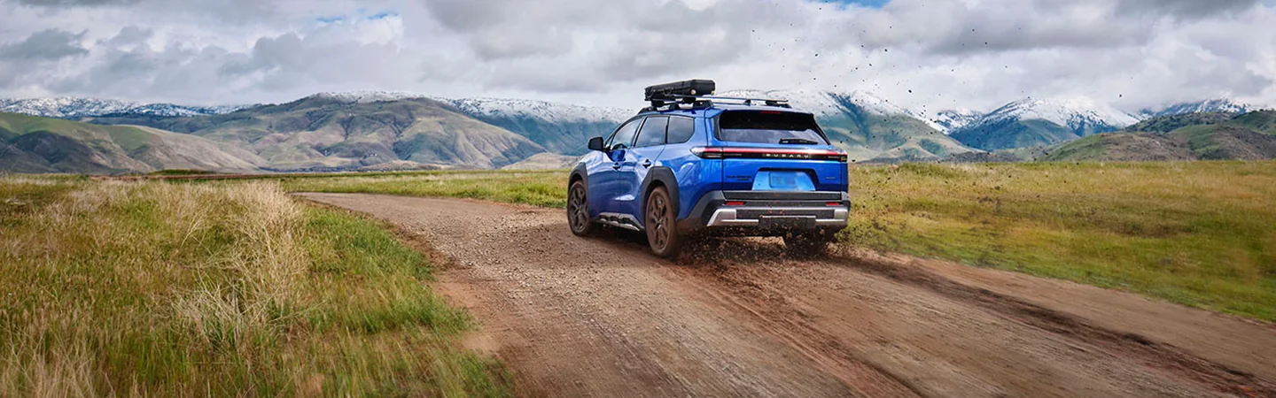 rear view of a blue 2026 Subaru Trailseeker Premium driving offroad spitting up dirt