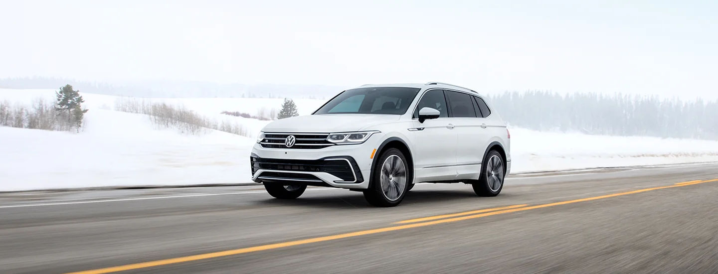 A white 2025 Volkswagen Tiguan driving next to a snowny field
