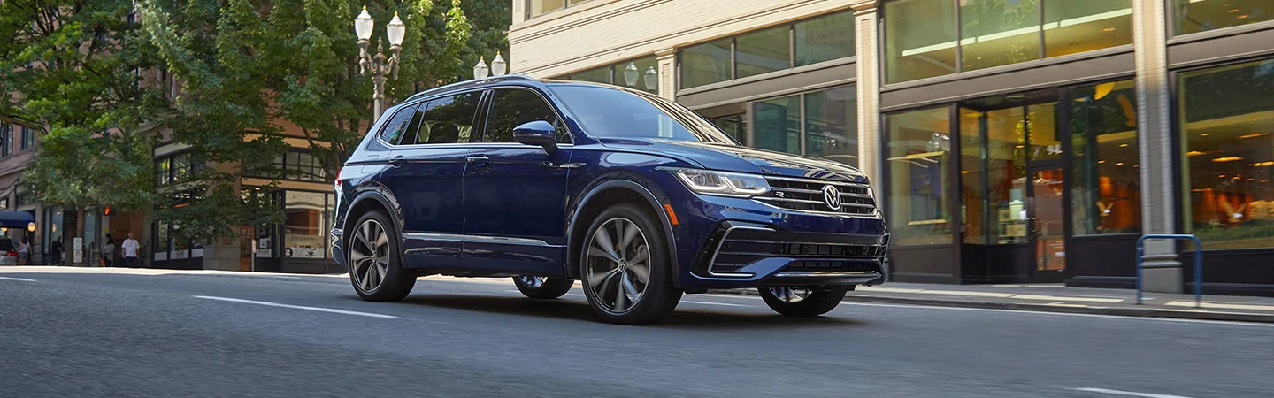 Side view of a blue 2025 Volkswagen Tiguan driving in the city