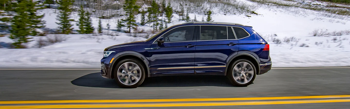 Side view of a blue 2025 Volkswagen Tiguan driving next to snow