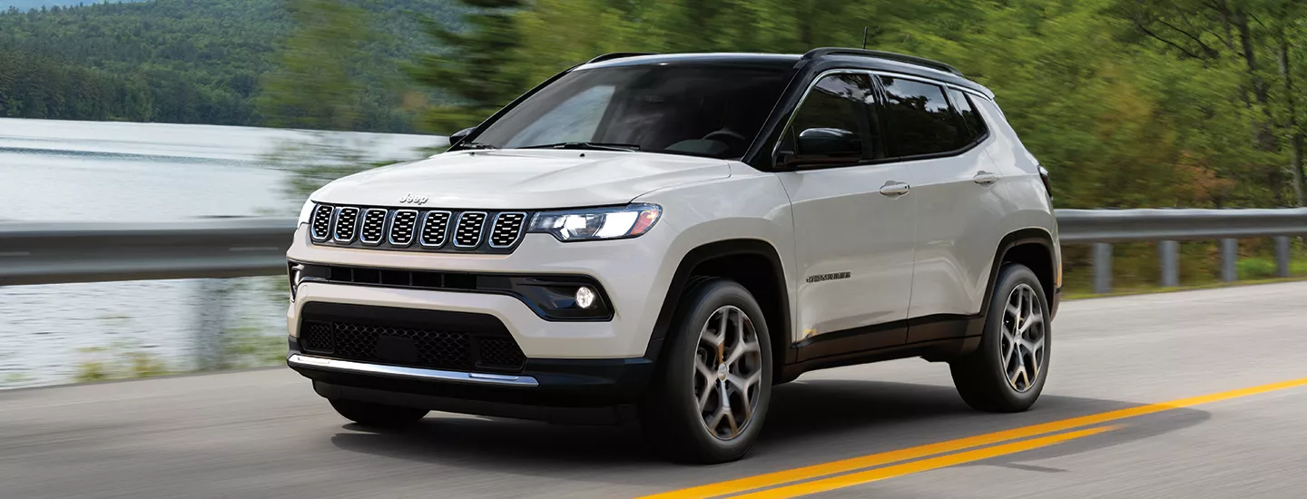 2025 Jeep Compass driving down a country road with a lake in the background