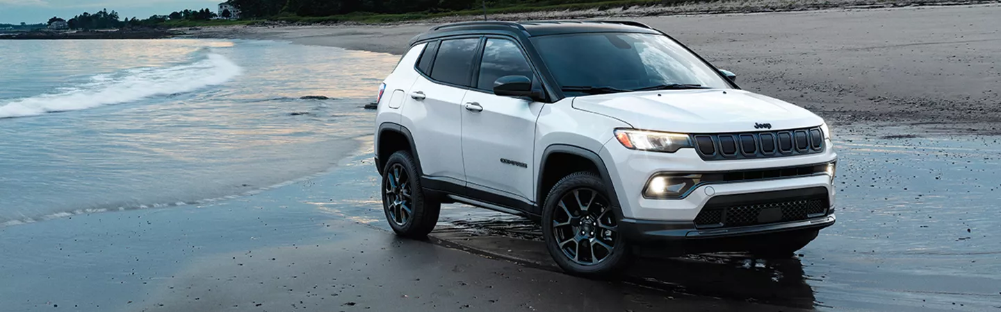 2025 Jeep Compass parked on the beach with trees and the ocean in the background