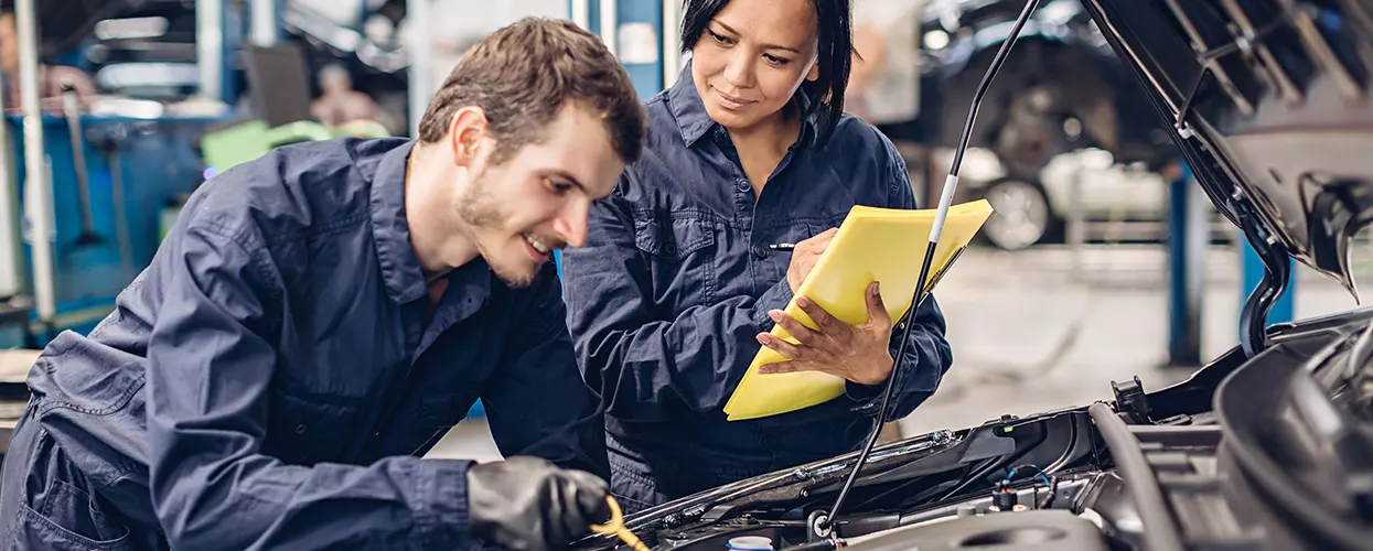 Two auto mechanics working on a car one with clipboard