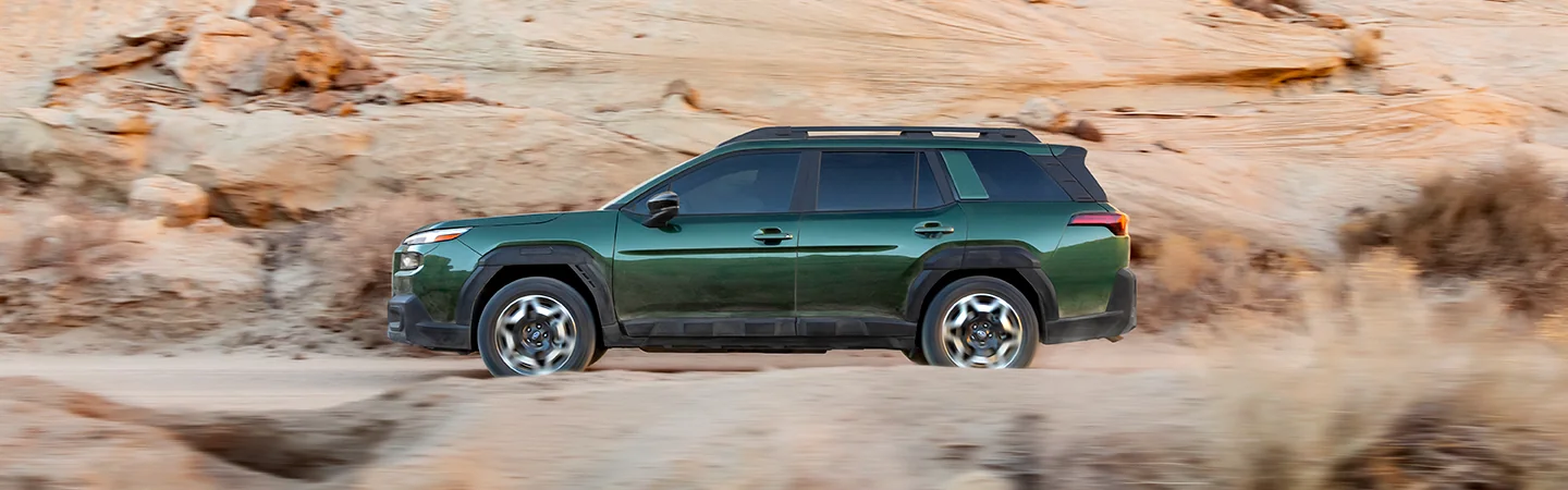 Side view of a green 2026 Subaru Outback Wilderness driving in the desert