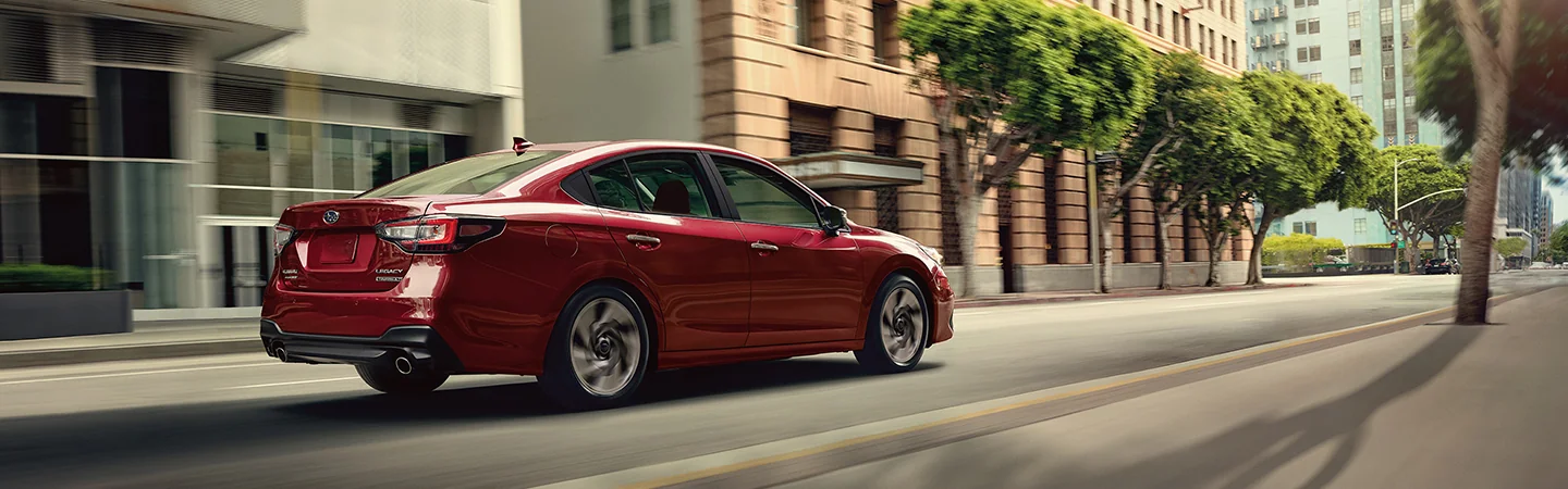 rear view of a red 2025 Subaru Legacy Touring XT drinbg in the city