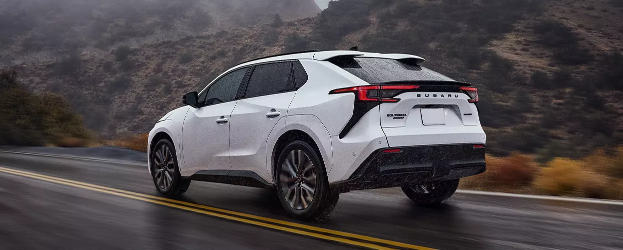 White Subaru Solterra electric SUV driving on a wet mountain road, showcasing all-electric performan…