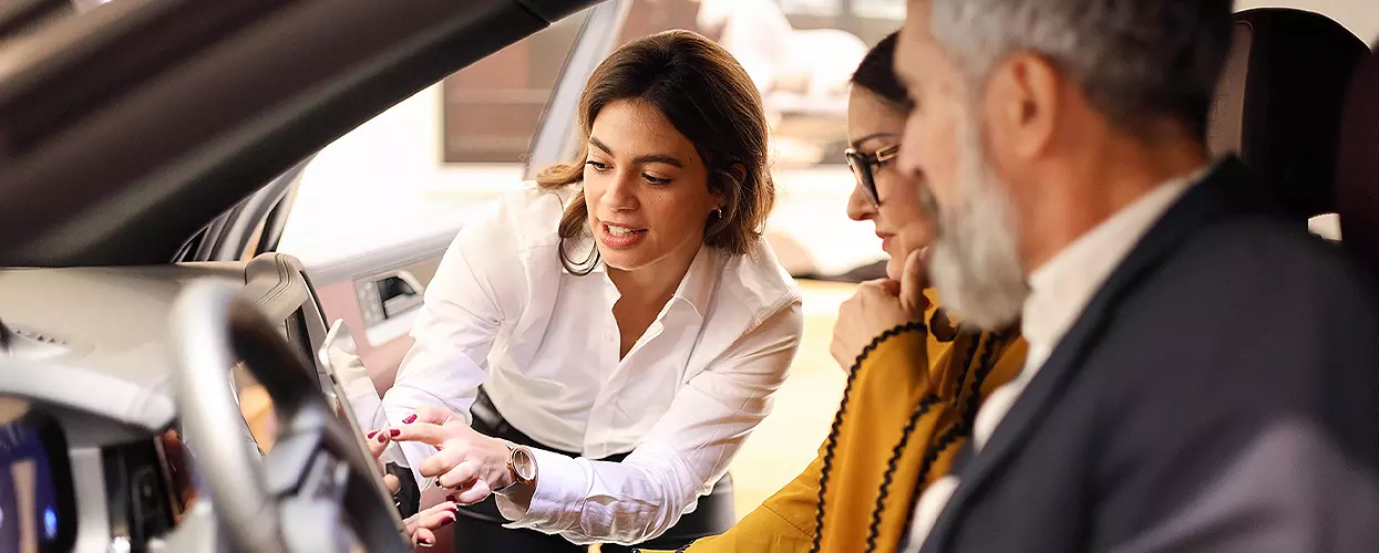 Car sales consultant demonstrating vehicle infotainment and technology features to customers during…