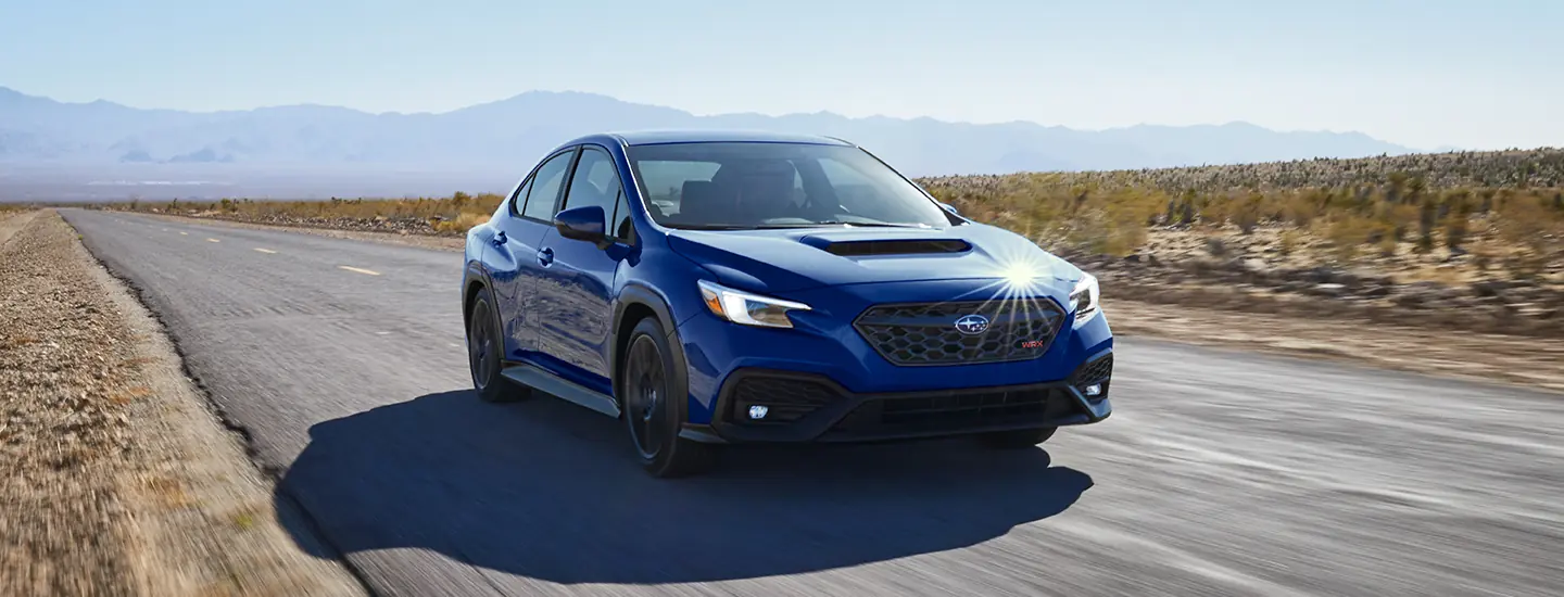Front view of a blue 2025 Subaru WRX driving on a road in the desert