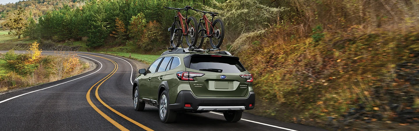 2025 Subaru Outback driving down a windy country road with bikes mounted on the roof