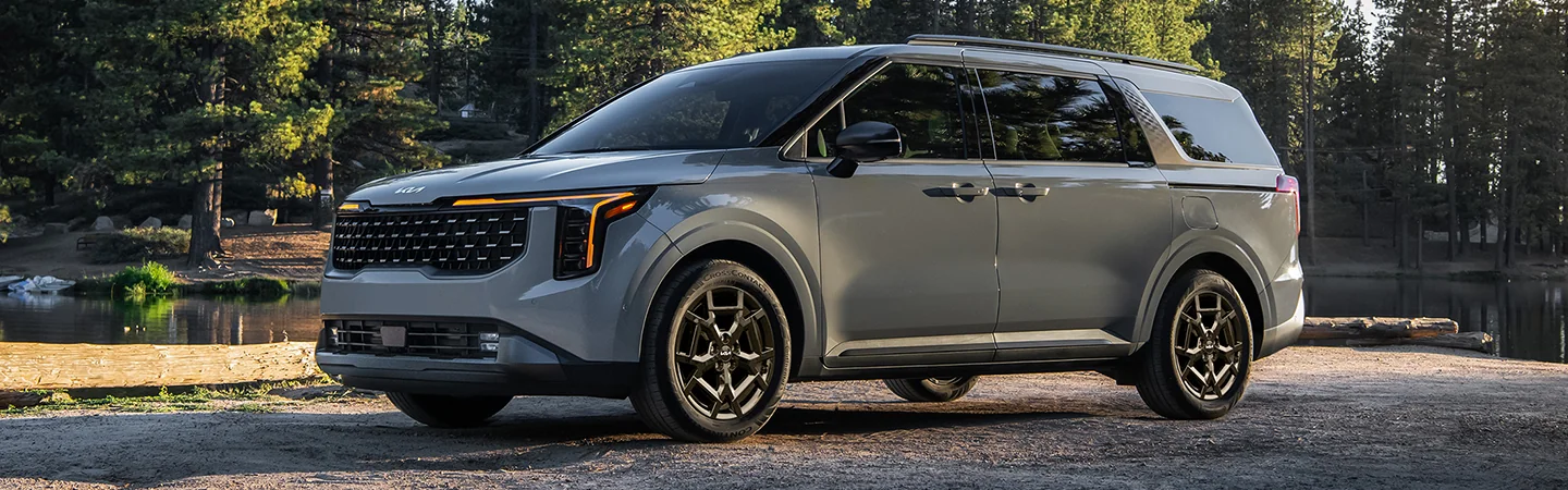 light gray 2025 Kia Carnival MPV Hybrid LXS parked by a lake