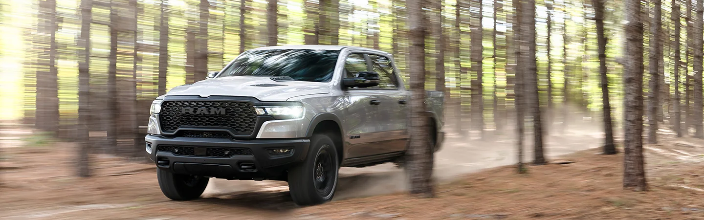 Front view of a gray 2026 RAM 1500 driving fast though a forest