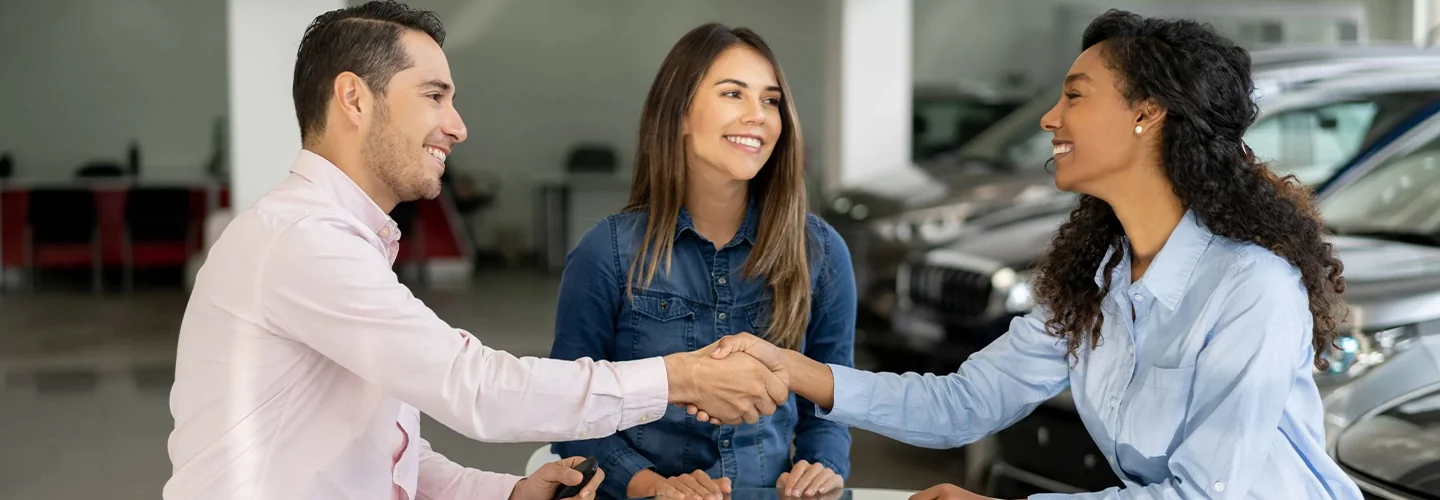 two people speakng to car dealer representative and shaking hands