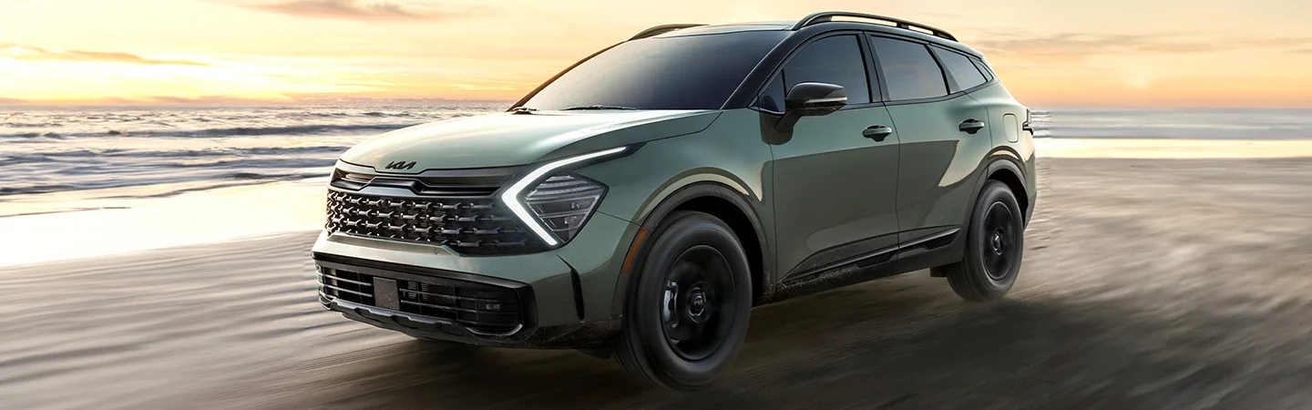 Front side view of a 2025 Kia Sportage driving on the beach